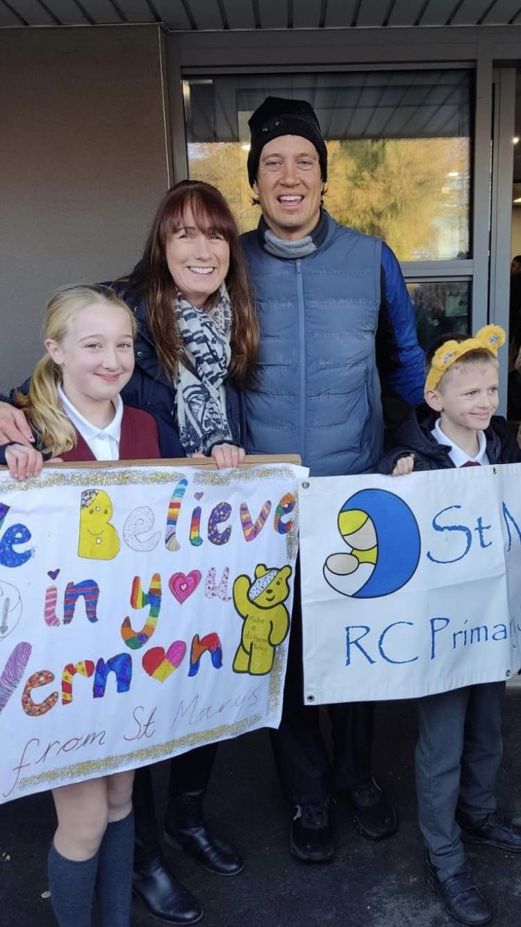 Vernon Kay stands with headteacher Dominique and two students. The pupils hold banners with well wishes to Vernon and their school banner