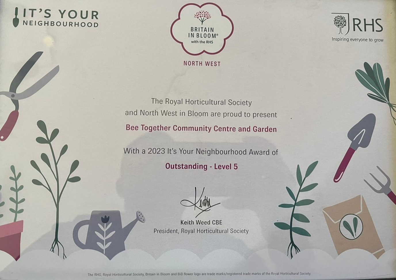 A photo of the award which says: The RHS and North West in Bloom are proud to present Bee Together Community Centre and Garden with a 2023 It's Your Neighbourhood Award of Outstanding - Level 5