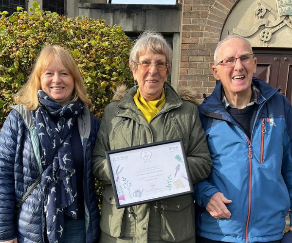 Pauline Riley holds the Bee Together Community Garden award with two volunteers either side