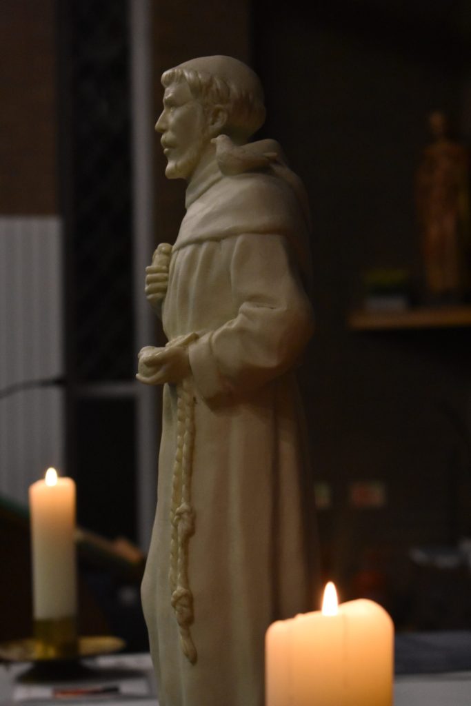 A statue of St Francis of Assisi again a dark background with two candles lit either side.