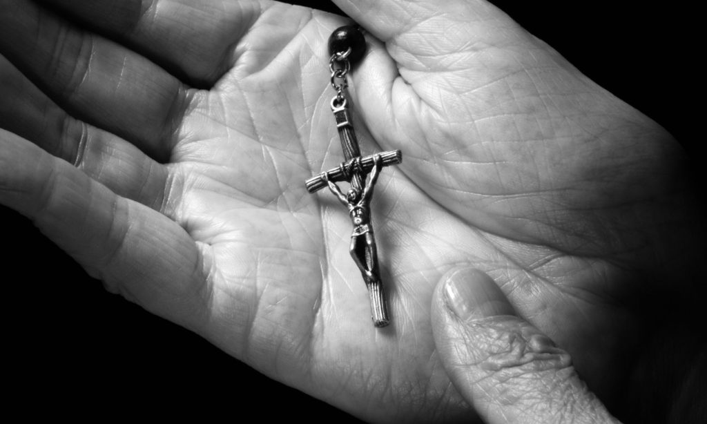 Black and white image of a crucifix in the palm of a hand